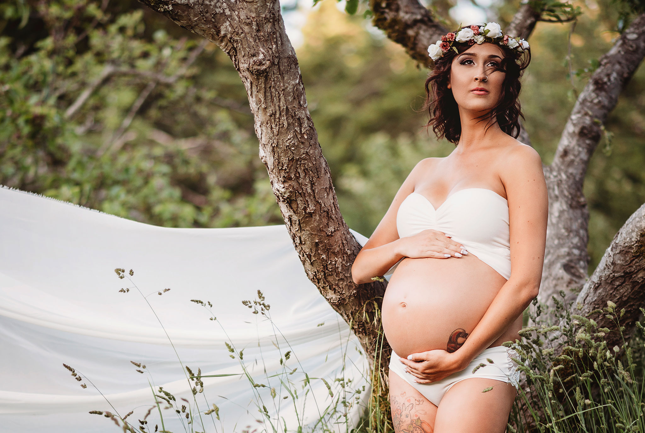 Maternity photography with flowing white maternity gown and flower crown at East Sooke Park near Victoria.