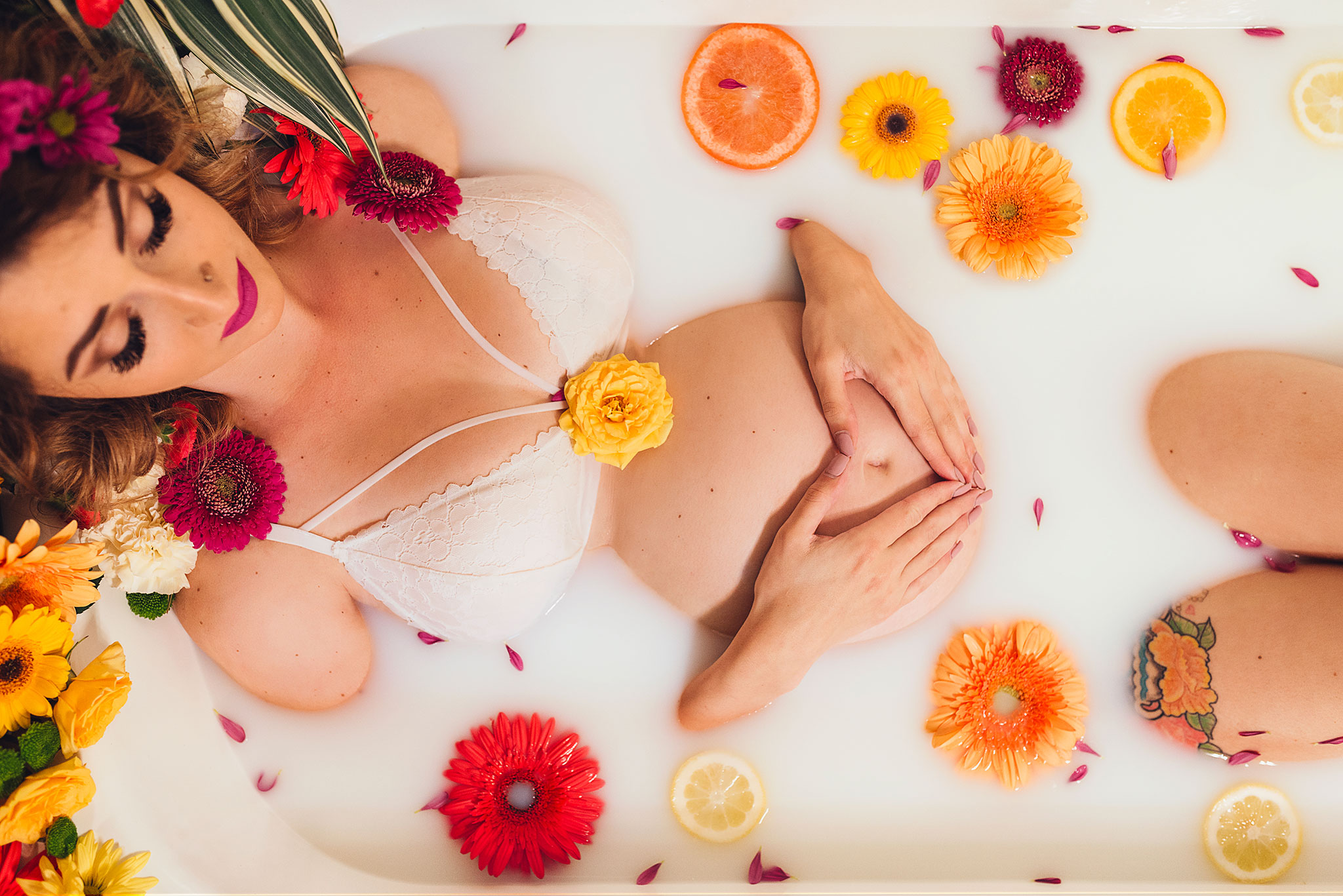Milk bath maternity photography with brightly coloured flowers and citrus.